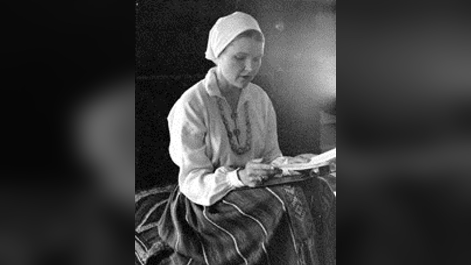 Aija Veldre Beldavs in Latvian folk dress, head bowed over her reading